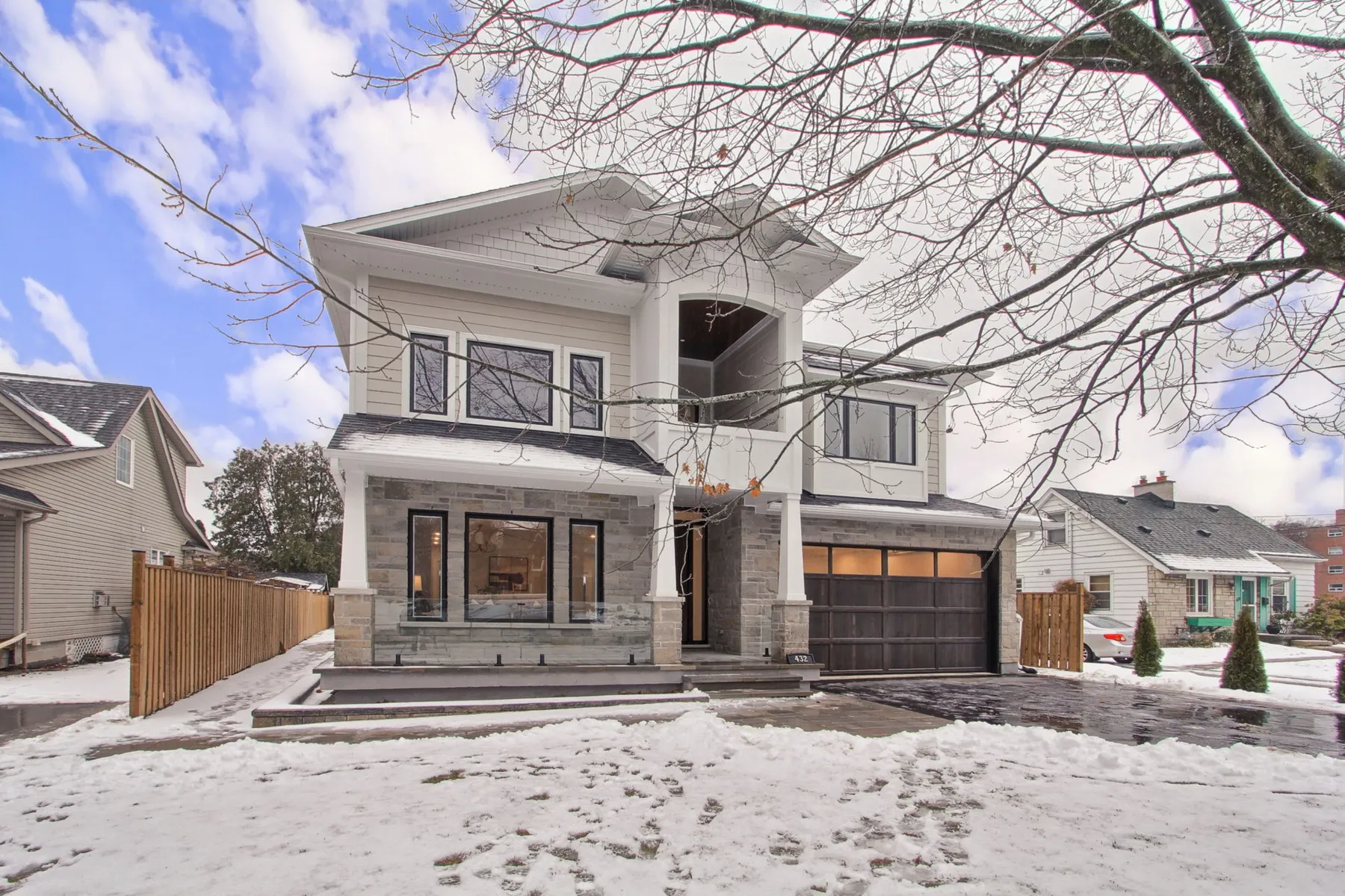 A two-storey custom home with pale grey siding, natural stone porch columns and black-framed windows