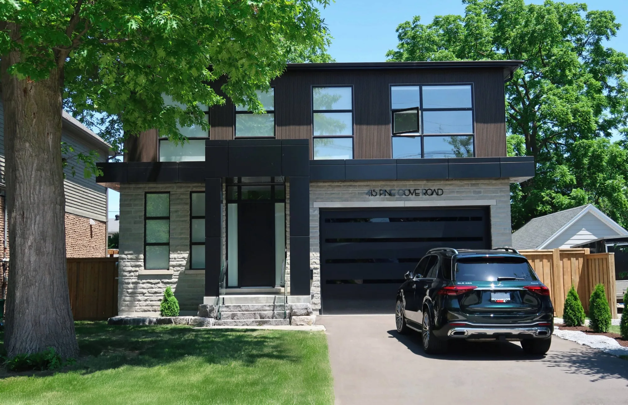 A modern two-storey custom home with a grey limestone base and dark vertical cladding