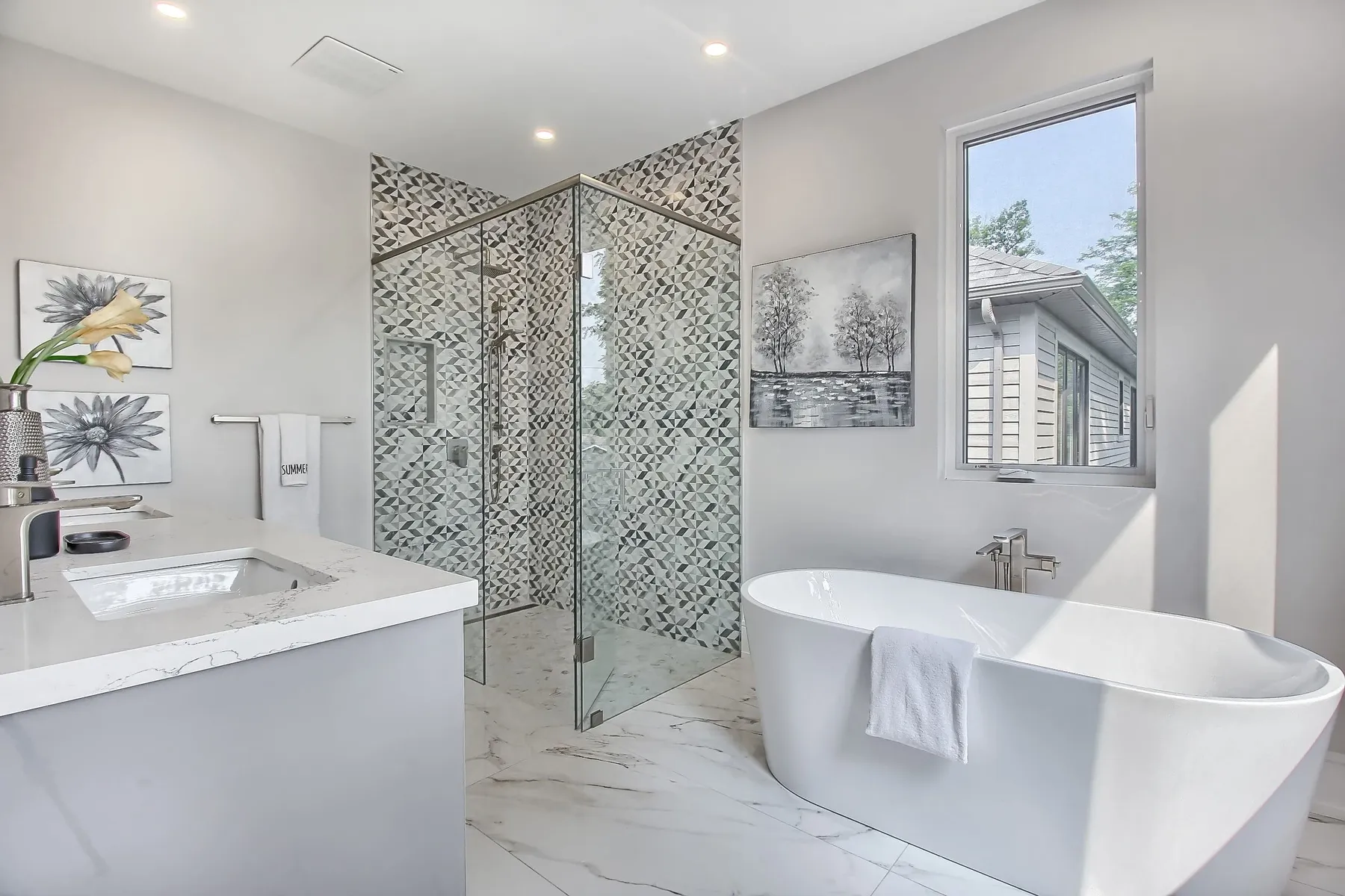 A spa-style bathroom with a freestanding soaker tub, a glass shower clad in grey mosaic tile and a quartz vanity