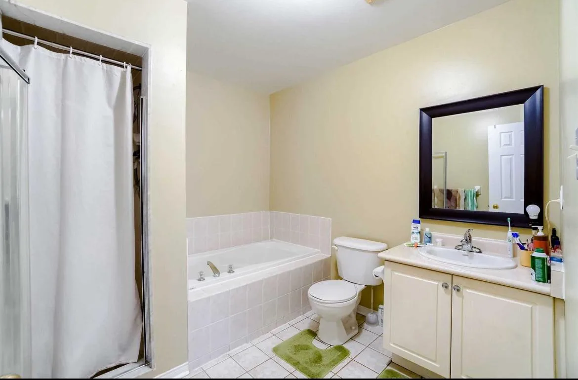 The bathroom before renovation: pale yellow walls, a white drop-in tub, an almond vanity and a curtained shower stall