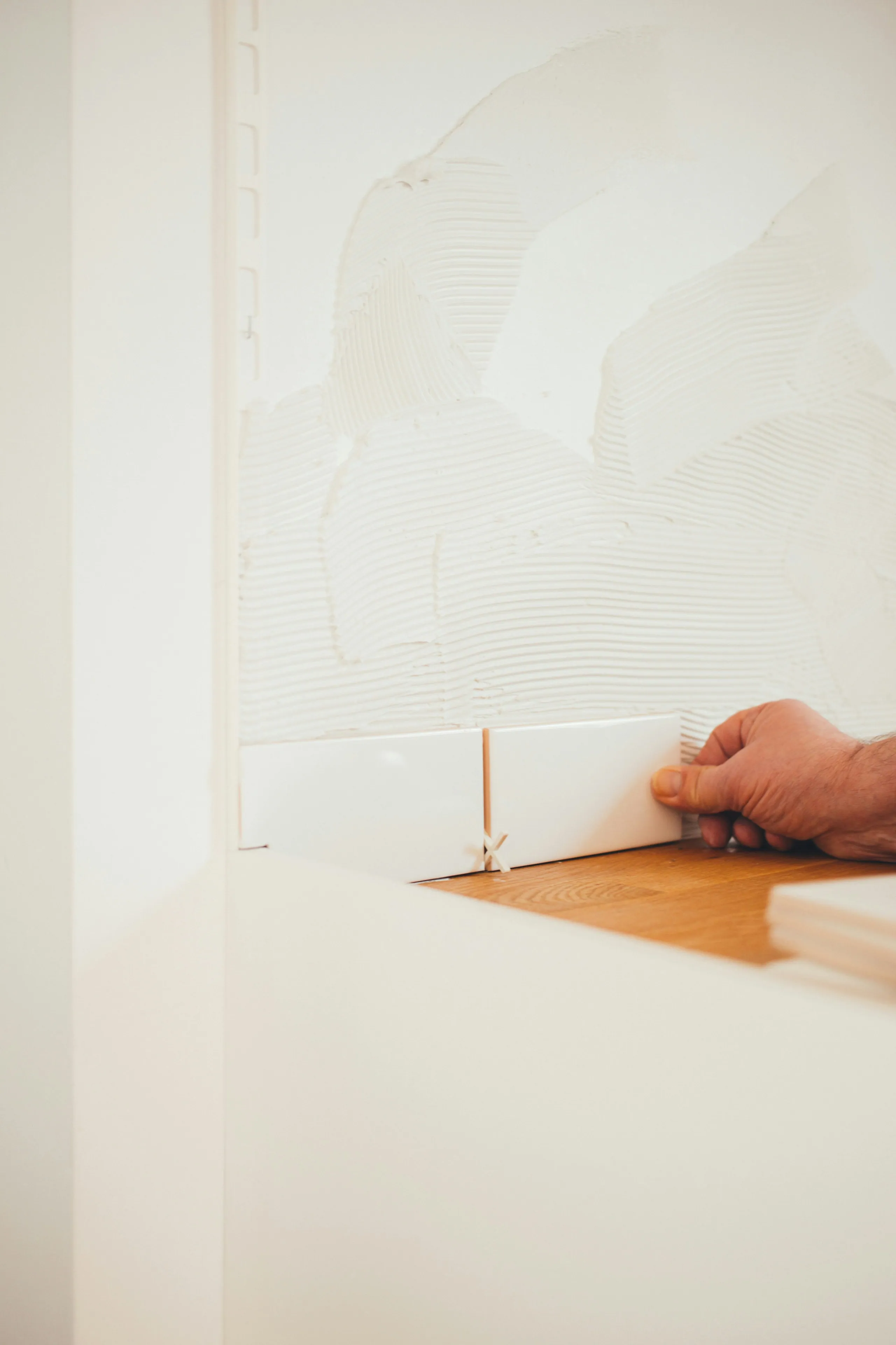 A hand setting white wall tile during an Oakville renovation